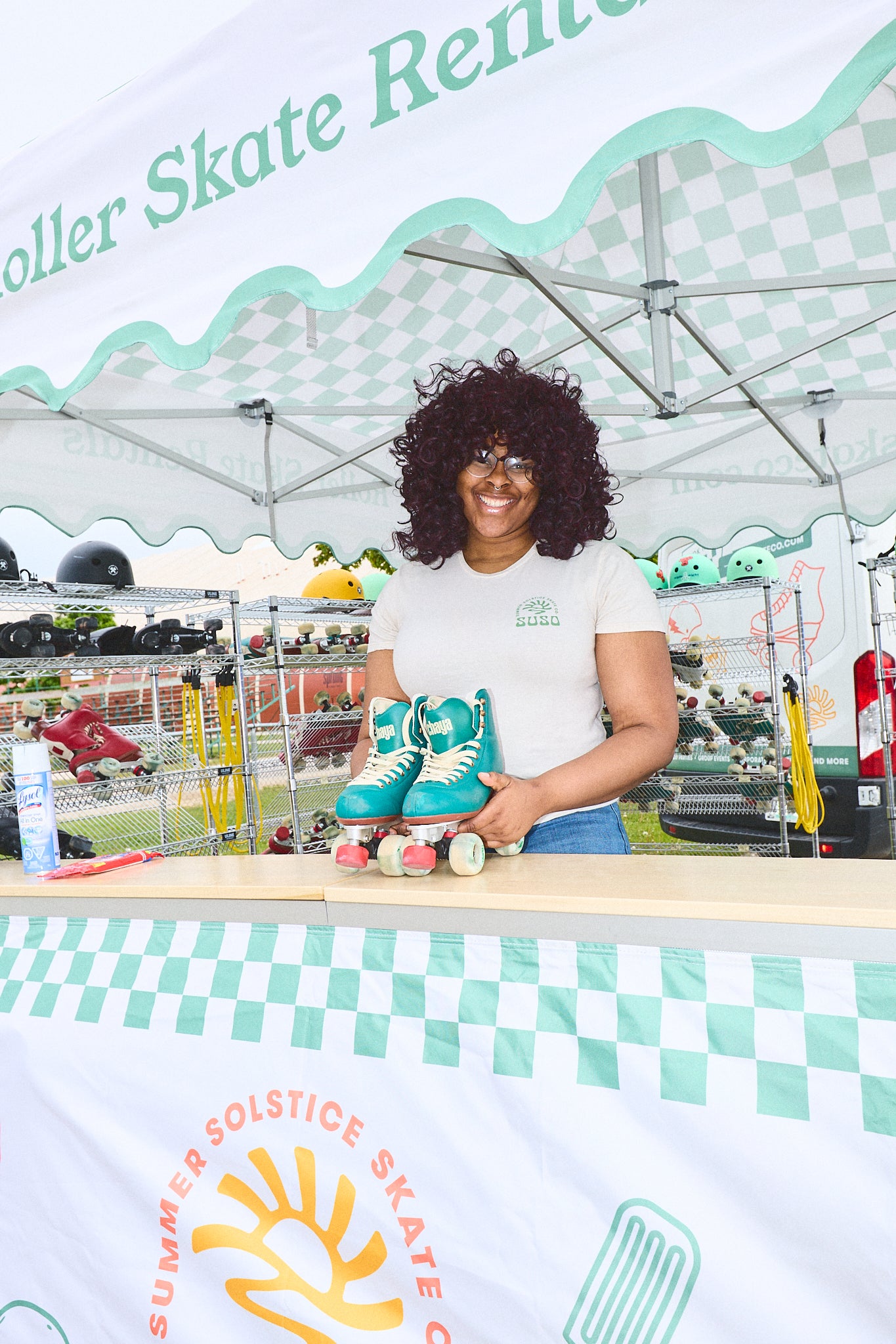 Woman holding roller skates at a Summer Solstice Skate event with a tent and skate rentals in the background.